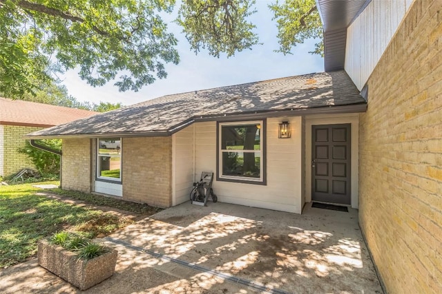 10108 Osprey Ct, Austin, TX 78750 - view of exterior entry featuring brick siding, roof with shingles, and a patio