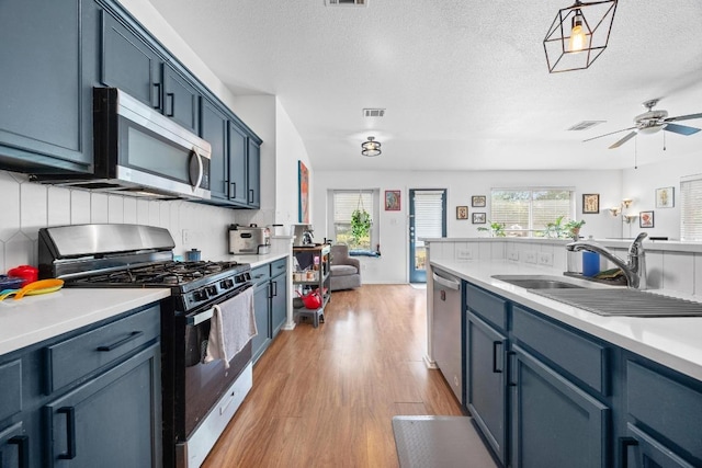 1112 Battenburg Trl, Pflugerville, TX 78660 - kitchen featuring appliances with stainless steel finishes, light wood-style floors, a ceiling fan, light countertops, and a textured ceiling