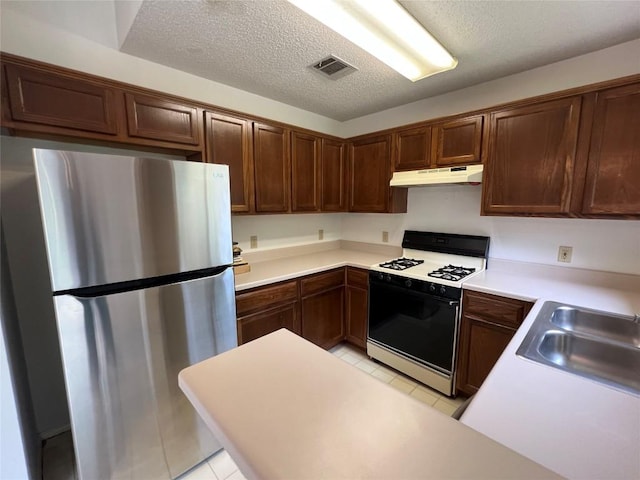 6612 Zequiel Dr, Austin, TX 78744 - kitchen with freestanding refrigerator, gas range oven, under cabinet range hood, light tile patterned floors, and a sink