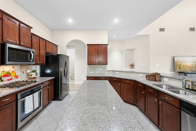 21105 Huckabee Bnd, Pflugerville, TX 78660 - kitchen with stainless steel appliances, a sink, arched walkways, light tile patterned floors, and light stone counters