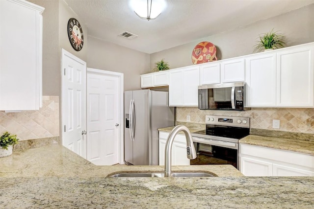 1003 E 3rd St, Georgetown, TX 78626 - kitchen featuring appliances with stainless steel finishes, light stone countertops, decorative backsplash, white cabinetry, and a sink