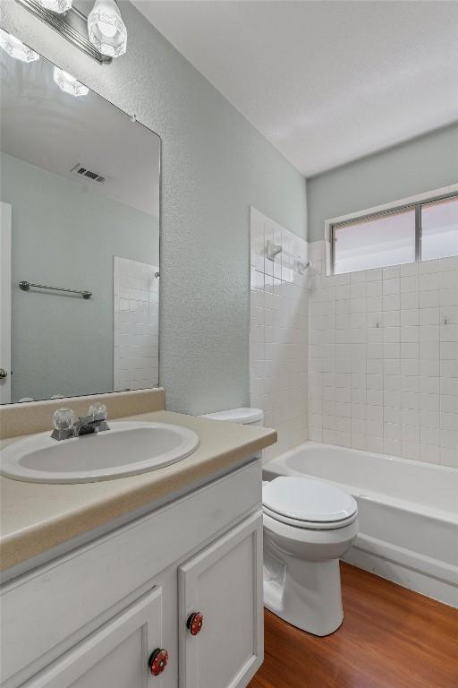 1011 Moser River Dr, Leander, TX 78641 - bathroom featuring wood finished floors, vanity, shower / washtub combination, toilet, and a textured wall