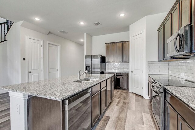 1905 Mariann Dr, Leander, TX 78641 - kitchen featuring appliances with stainless steel finishes, light wood-style flooring, light stone counters, a kitchen island with sink, and recessed lighting