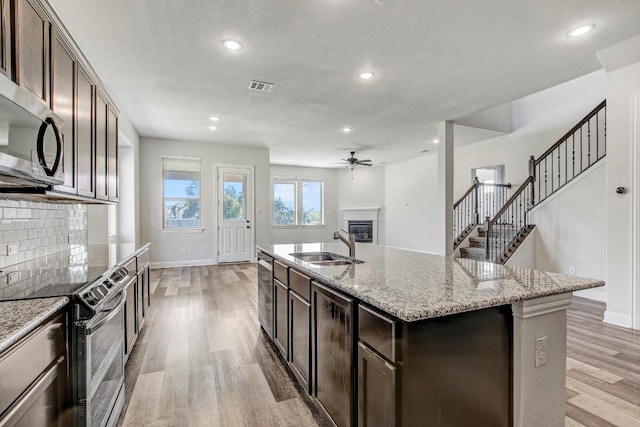 1905 Mariann Dr, Leander, TX 78641 - kitchen with stainless steel appliances, a glass covered fireplace, light wood-style flooring, ceiling fan, and recessed lighting