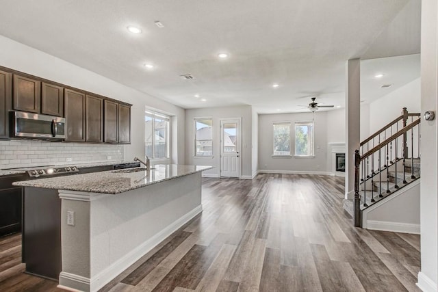 1905 Mariann Dr, Leander, TX 78641 - kitchen featuring stainless steel microwave, ceiling fan, dark brown cabinetry, dark wood finished floors, and a kitchen island with sink