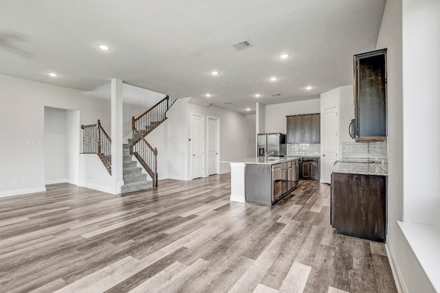 1905 Mariann Dr, Leander, TX 78641 - kitchen featuring stainless steel fridge, light wood-style flooring, a kitchen island with sink, dark brown cabinets, and recessed lighting