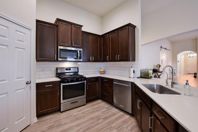 216 Walkup Ln, Leander, TX 78641 - kitchen featuring appliances with stainless steel finishes, a sink, arched walkways, light countertops, and light wood-type flooring