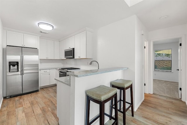 2205 Thornwild Pass, Austin, TX 78758 - kitchen featuring appliances with stainless steel finishes, light wood-style flooring, a peninsula, white cabinetry, and a kitchen breakfast bar