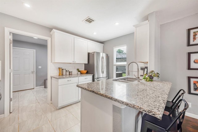 1906 Garden Villa Dr, Georgetown, TX 78628 - kitchen featuring freestanding refrigerator, light stone countertops, white cabinetry, a kitchen breakfast bar, and a peninsula