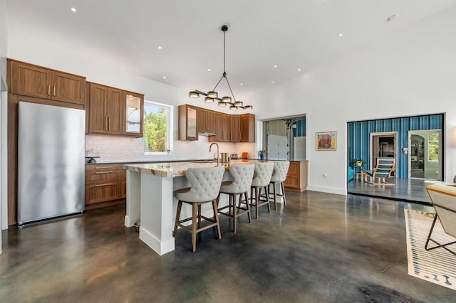 2300 Stagecoach Ranch Loop Unit B, Dripping Springs, TX 78620 - kitchen featuring freestanding refrigerator, concrete flooring, brown cabinetry, a sink, and an island with sink
