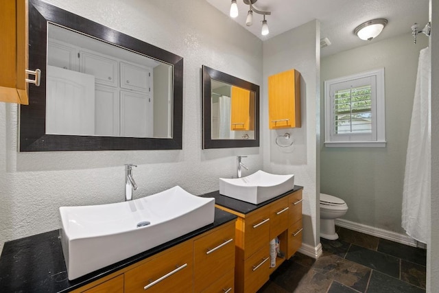 13201 Stillforest St, Austin, TX 78729 - bathroom with double vanity, stone tile floors, toilet, baseboards, and a textured wall
