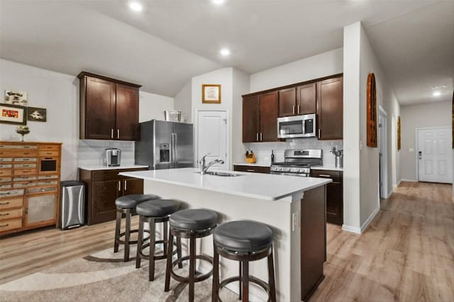 320 Bright Star Ln, Georgetown, TX 78628 - kitchen featuring stainless steel appliances, a sink, light wood-type flooring, backsplash, and a kitchen breakfast bar