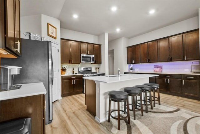 320 Bright Star Ln, Georgetown, TX 78628 - kitchen featuring appliances with stainless steel finishes, light wood-style floors, a breakfast bar area, a kitchen island with sink, and dark brown cabinetry