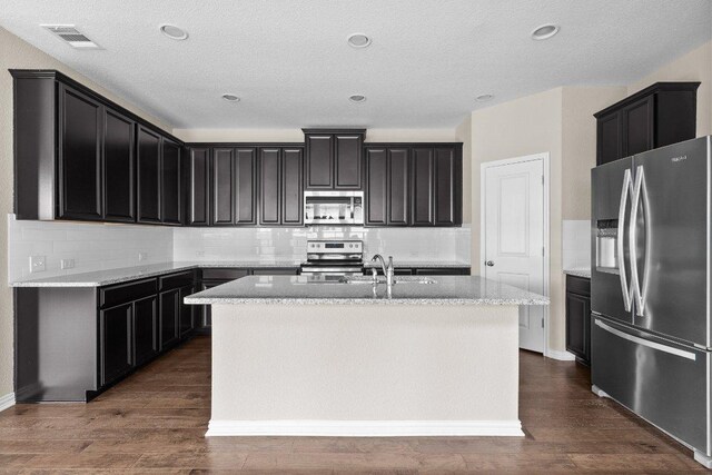 202 Westfield St, Hutto, TX 78634 - kitchen with stainless steel appliances, an island with sink, backsplash, dark wood-style floors, and a textured ceiling
