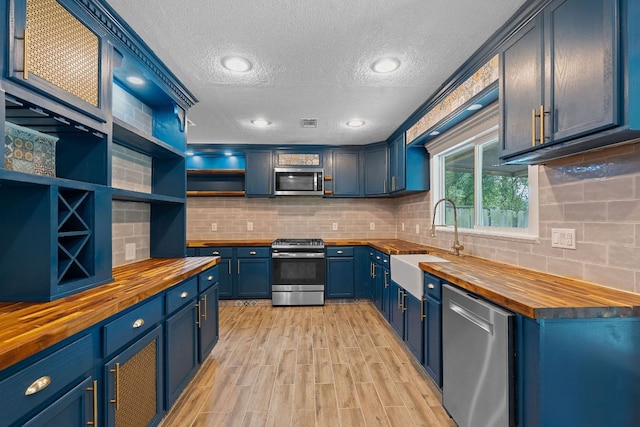1515 Mearns Meadow Blvd, Austin, TX 78758 - kitchen with butcher block counters, appliances with stainless steel finishes, a sink, blue cabinets, and a textured ceiling
