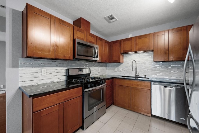 5601 Samuel Huston Ave, Austin, TX 78721 - kitchen featuring stainless steel appliances, tasteful backsplash, light tile patterned flooring, brown cabinets, and a textured ceiling