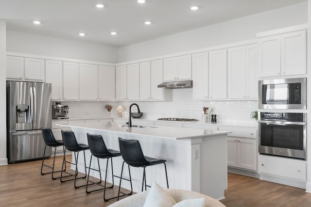 256 Smoke Tree Cir, Dripping Springs, TX 78620 - kitchen featuring stainless steel appliances, a sink, under cabinet range hood, a kitchen island with sink, and light countertops