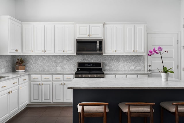 1518 Frontier Valley Dr, Austin, TX 78741 - kitchen with appliances with stainless steel finishes, a breakfast bar area, dark tile patterned flooring, and white cabinetry