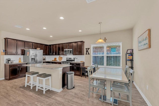409 Red Matador Ln, Leander, TX 78641 - kitchen featuring appliances with stainless steel finishes, a sink, dark brown cabinets, light wood-style flooring, and an island with sink
