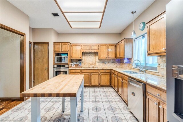 336 Primrose Dr, Kyle, TX 78640 - kitchen featuring appliances with stainless steel finishes, a sink, decorative backsplash, decorative light fixtures, and brown cabinetry