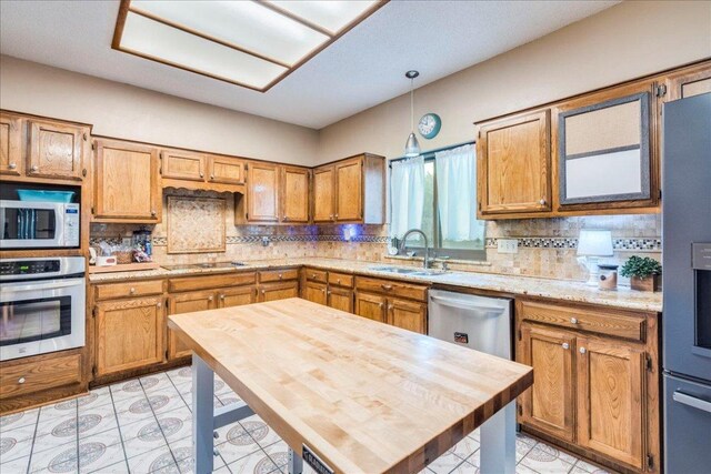 336 Primrose Dr, Kyle, TX 78640 - kitchen featuring appliances with stainless steel finishes, a sink, light countertops, backsplash, and brown cabinetry