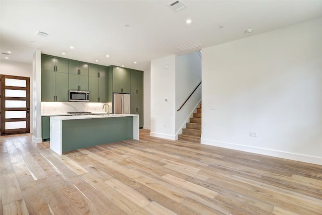 3208 Clawson Rd Unit 3A, Austin, TX 78704 - kitchen featuring appliances with stainless steel finishes, green cabinets, light wood finished floors, light countertops, and a kitchen island with sink