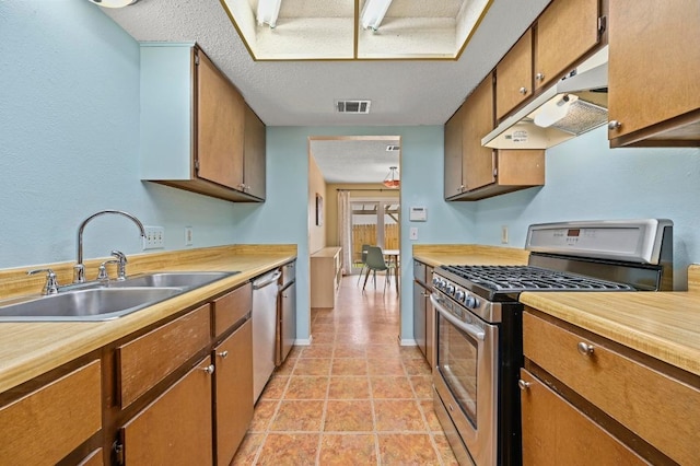 3921 Leafield Dr, Austin, TX 78749 - kitchen with stainless steel appliances, under cabinet range hood, light countertops, brown cabinetry, and a textured ceiling