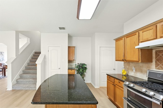 1113 Red Ranch Cir, Cedar Park, TX 78613 - kitchen featuring range with two ovens, light wood finished floors, under cabinet range hood, decorative backsplash, and dark stone countertops