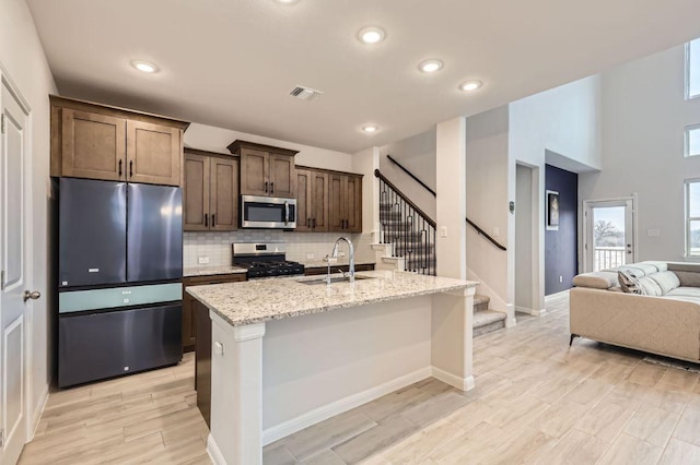 149 Woods Edge Ln, Georgetown, TX 78628 - kitchen featuring stainless steel appliances, a sink, backsplash, light stone counters, and an island with sink