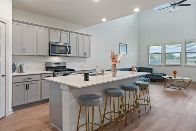 13705 Mc Arthur Dr, Manor, TX 78653 - kitchen featuring stainless steel appliances, gray cabinetry, a sink, open floor plan, and light wood-style floors