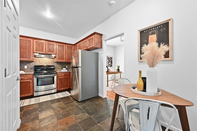 1169 Curve St, Austin, TX 78702 - kitchen with stainless steel appliances, under cabinet range hood, stone finish floors, decorative backsplash, and brown cabinets