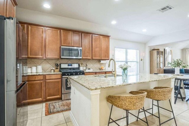 340 Beretta Cir, Georgetown, TX 78628 - kitchen featuring stainless steel appliances, a sink, tasteful backsplash, brown cabinetry, and light stone countertops