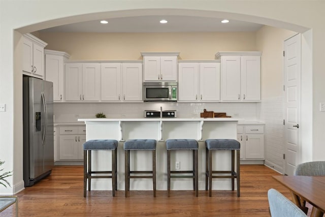 20213 Hidden Gully Ln, Pflugerville, TX 78660 - kitchen featuring appliances with stainless steel finishes, white cabinetry, a breakfast bar, arched walkways, and recessed lighting