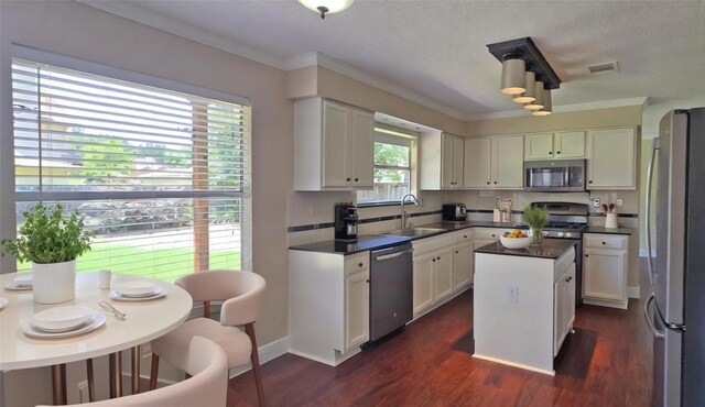 kitchen with stainless steel appliances, a sink, white cabinetry, a kitchen island, and crown molding