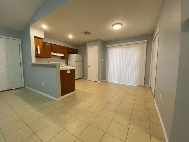 1402 Waterloo Trl, Austin, TX 78704 - kitchen featuring freestanding refrigerator, under cabinet range hood, a peninsula, light countertops, and light tile patterned floors