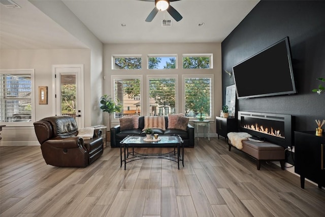 5820 Harper Park Dr Unit 66, Austin, TX 78735 - living room featuring healthy amount of natural light, a ceiling fan, wood finished floors, and a warm lit fireplace