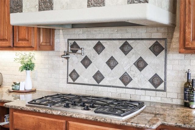 17400 Northlake Hills Dr, Jonestown, TX 78645 - kitchen featuring stainless steel gas stovetop, brown cabinetry, tasteful backsplash, and light stone counters