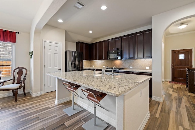 1049 Naranjo Dr, Georgetown, TX 78628 - kitchen featuring arched walkways, fridge with ice dispenser, black microwave, light wood finished floors, and recessed lighting