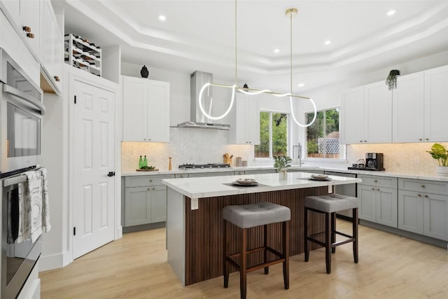14904 Cordero Dr, Austin, TX 78717 - kitchen with a raised ceiling, wall chimney range hood, gray cabinetry, light wood-style floors, and recessed lighting