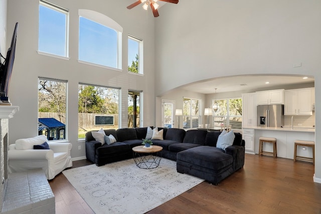 7221 Seneca Falls Loop, Austin, TX 78739 - living area with ceiling fan, arched walkways, a towering ceiling, a brick fireplace, and dark wood-style floors