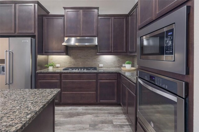 204 Hopping Peach St, San Marcos, TX 78666 - kitchen with appliances with stainless steel finishes, ventilation hood, dark stone counters, light wood finished floors, and decorative backsplash