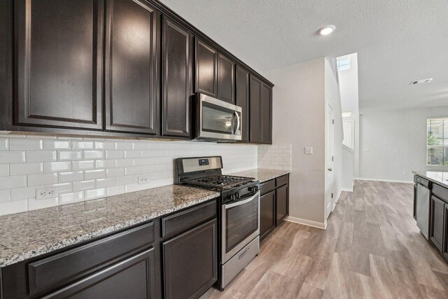 202 Delaware Mountains Ter, Dripping Springs, TX 78620 - kitchen featuring appliances with stainless steel finishes, light wood-type flooring, decorative backsplash, light stone countertops, and baseboards