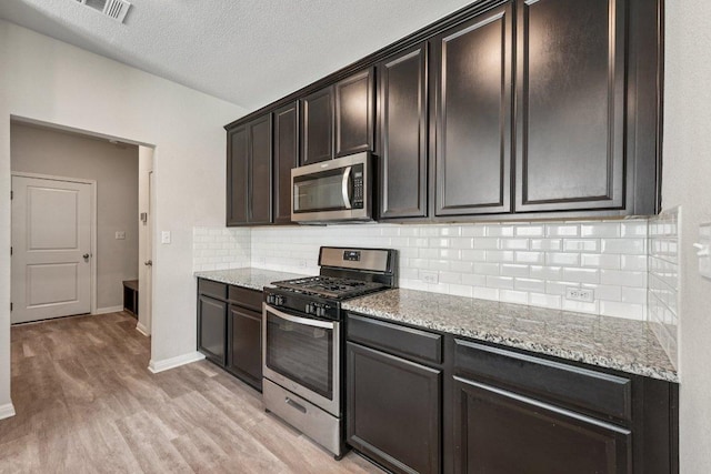 202 Delaware Mountains Ter, Dripping Springs, TX 78620 - kitchen with stainless steel appliances, light stone countertops, light wood-style flooring, backsplash, and a textured ceiling