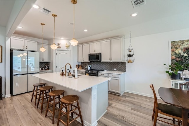 12904 Cerro Castellan Trce, Manor, TX 78653 - kitchen with appliances with stainless steel finishes, a sink, light wood finished floors, a kitchen bar, and backsplash