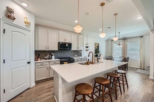12904 Cerro Castellan Trce, Manor, TX 78653 - kitchen with black gas stove, a sink, tasteful backsplash, light wood-type flooring, and a kitchen bar