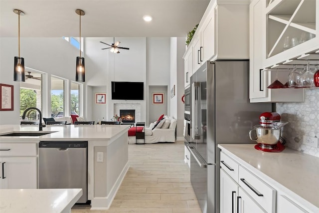 17804 Hattie Trce, Austin, TX 78738 - kitchen with appliances with stainless steel finishes, a sink, a ceiling fan, light wood-style flooring, and a glass covered fireplace