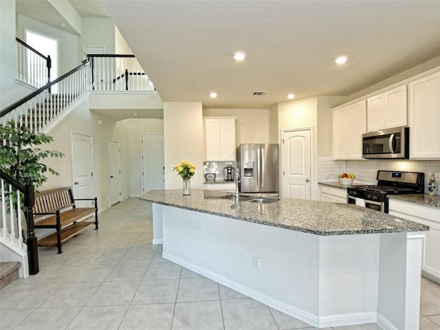 913 Swan Flower St, Leander, TX 78641 - kitchen with stainless steel appliances, a kitchen island with sink, stone countertops, tasteful backsplash, and white cabinets