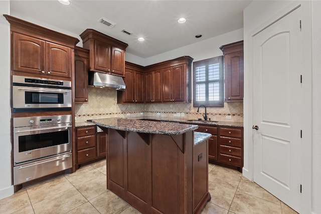 1036 Liberty Park Dr Unit 3, Austin, TX 78746 - kitchen featuring under cabinet range hood, light tile patterned floors, dark stone countertops, a warming drawer, and recessed lighting