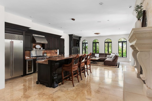 4256 Fischer Store Rd, Wimberley, TX 78676 - kitchen featuring stainless steel built in fridge, beverage cooler, a breakfast bar, wall chimney exhaust hood, and tasteful backsplash