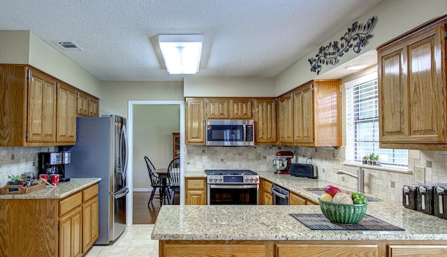 14309 Richard Walker Blvd, Austin, TX 78728 - kitchen with stainless steel appliances, a sink, a peninsula, tasteful backsplash, and a textured ceiling
